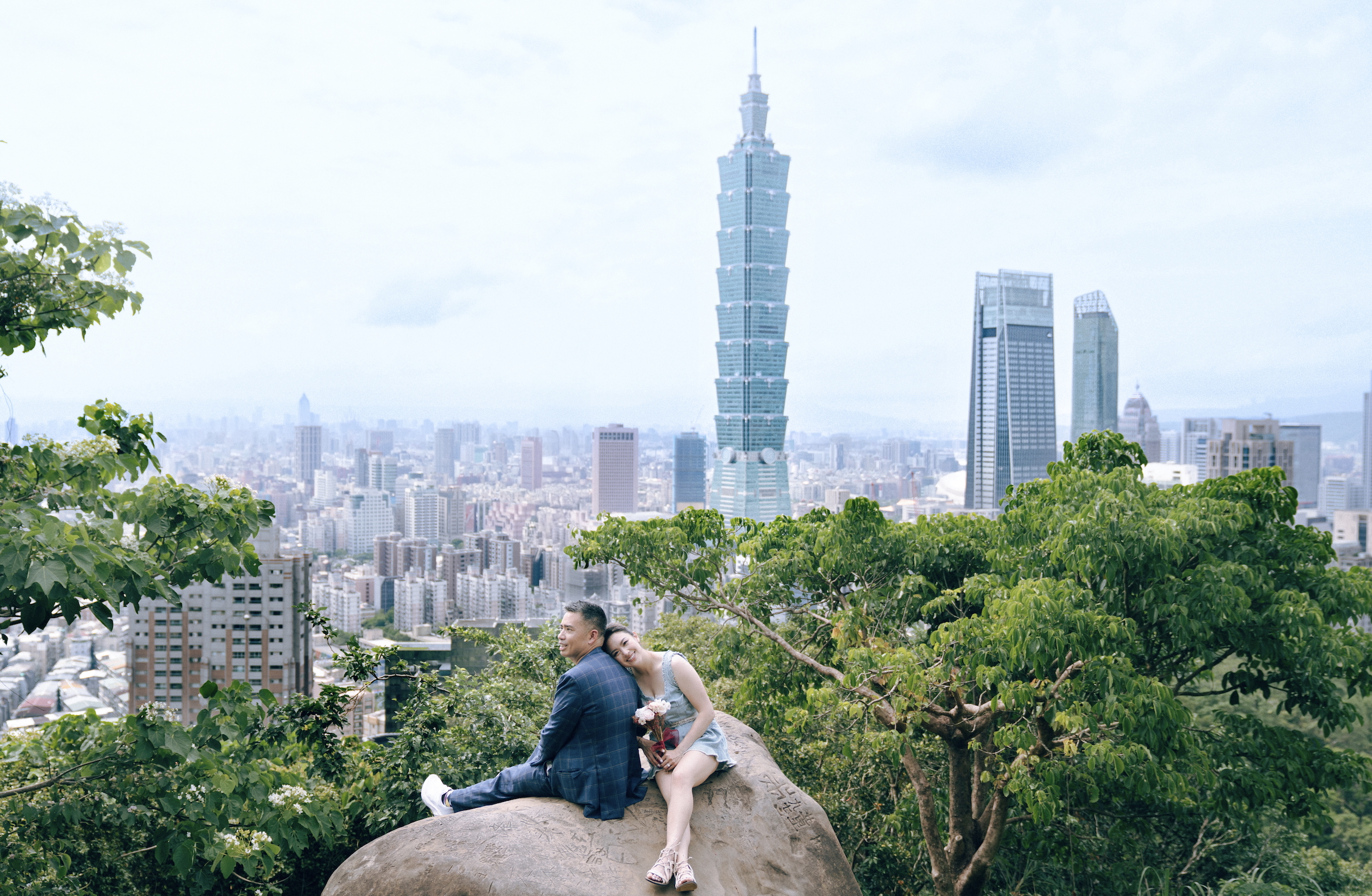 Max and Margaret sitting on a rock overlooking Taipei city with Taipei 101 in the background